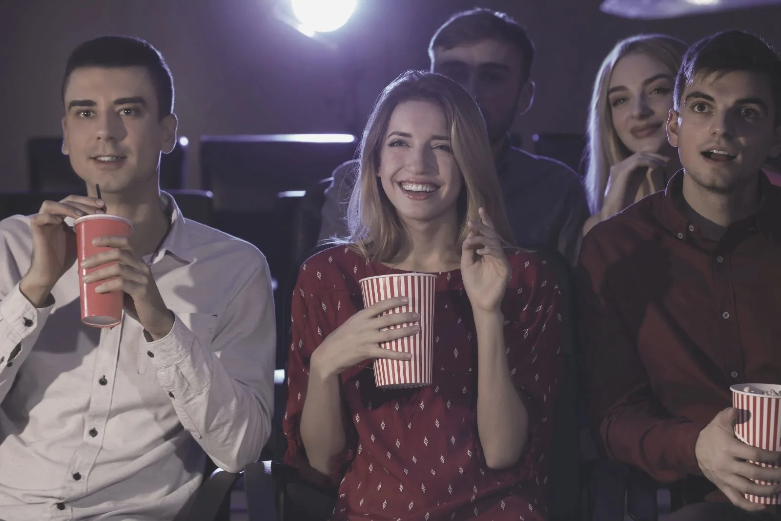 men and women watching movie in the cinema laughing and eating food