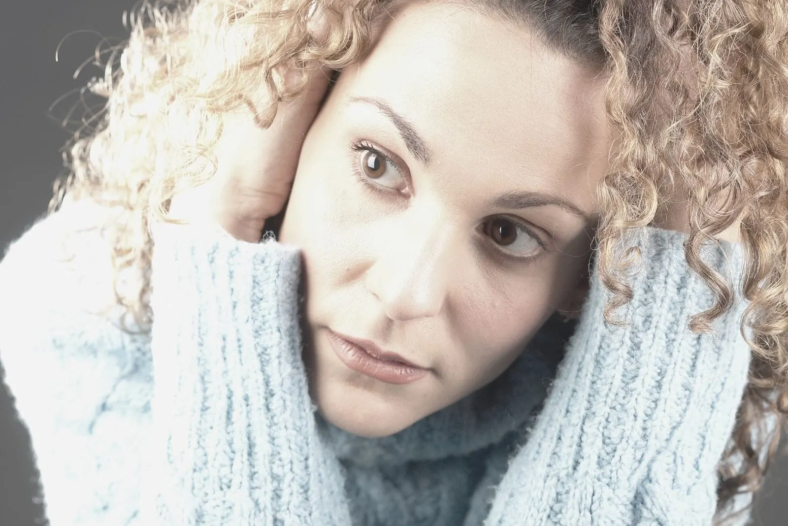 mid adult woman thinking deeply holding her blonde curly hair looking away in close up image
