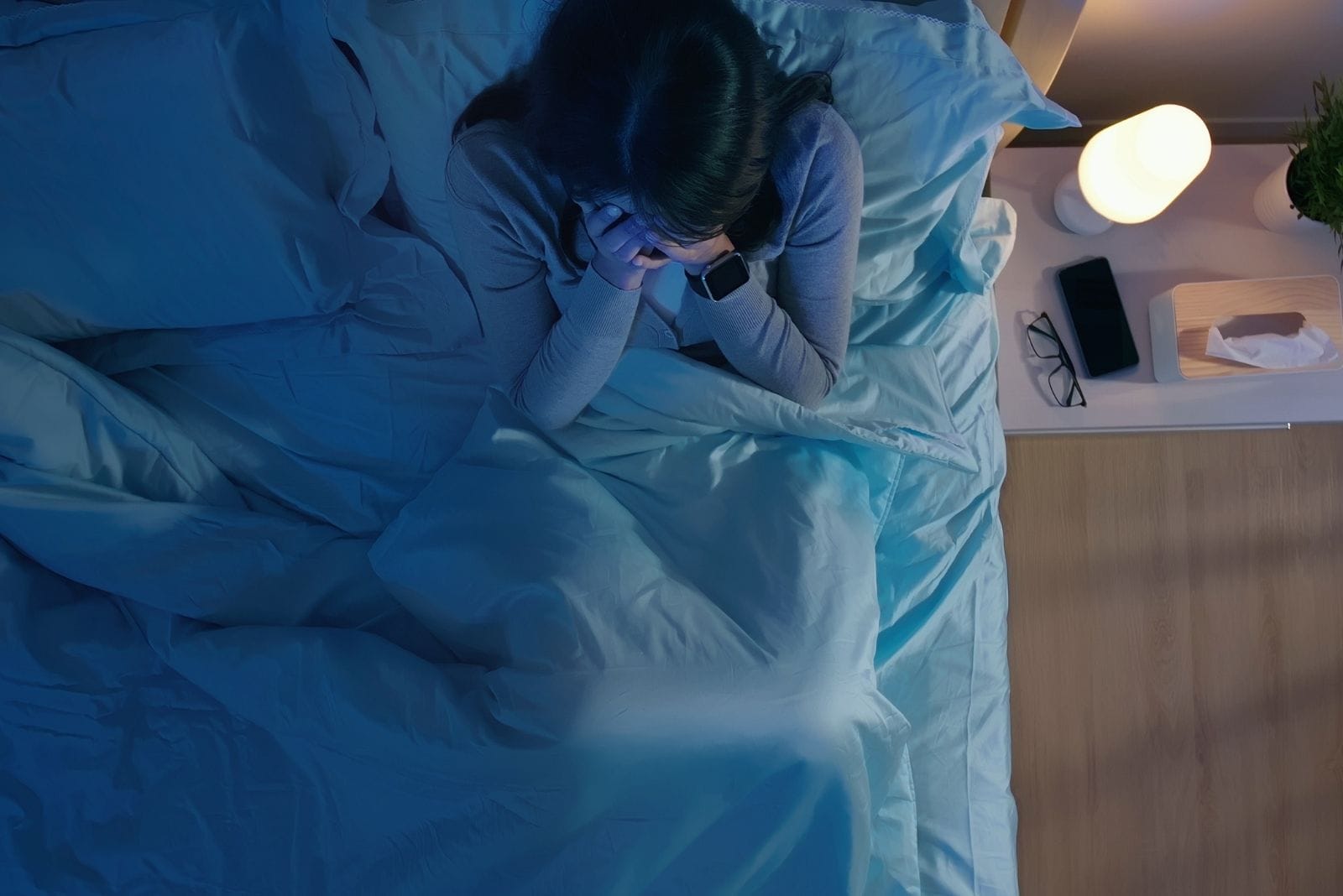 Ripresa dall'alto di una donna asiatica seduta a letto a tarda notte che si copre il viso con le mani