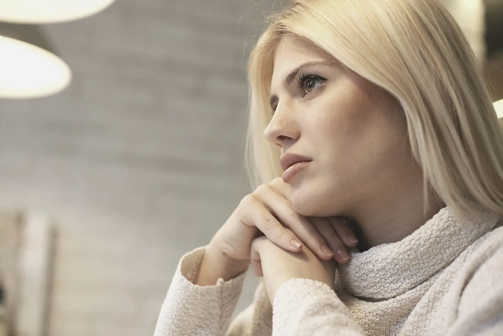 pensive and young lady sitting with blonde straight hair and head leaning on both hands in low angle