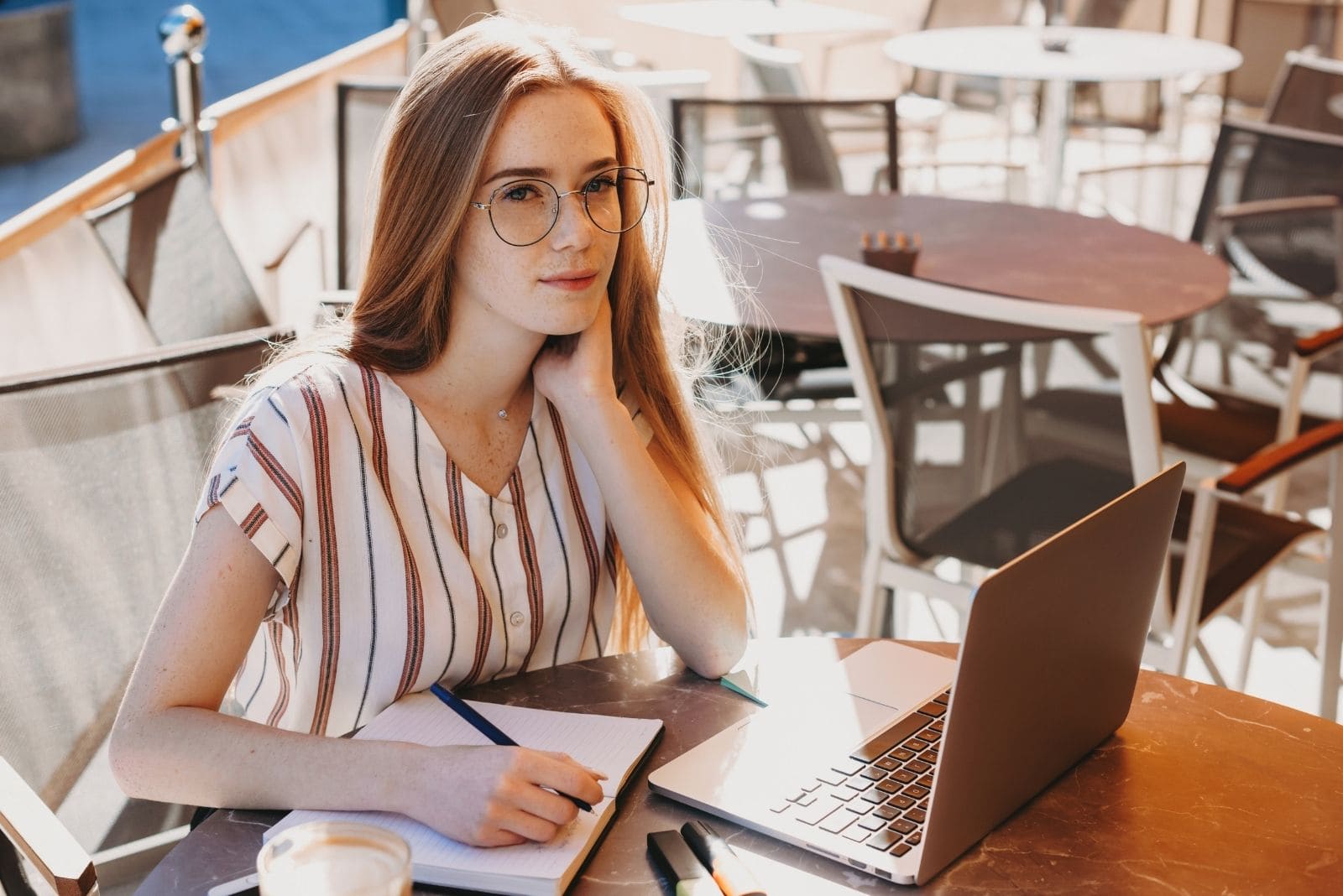 Donna d'affari pensierosa che scrive al tavolo di un caffè all'aperto con un computer portatile in testa