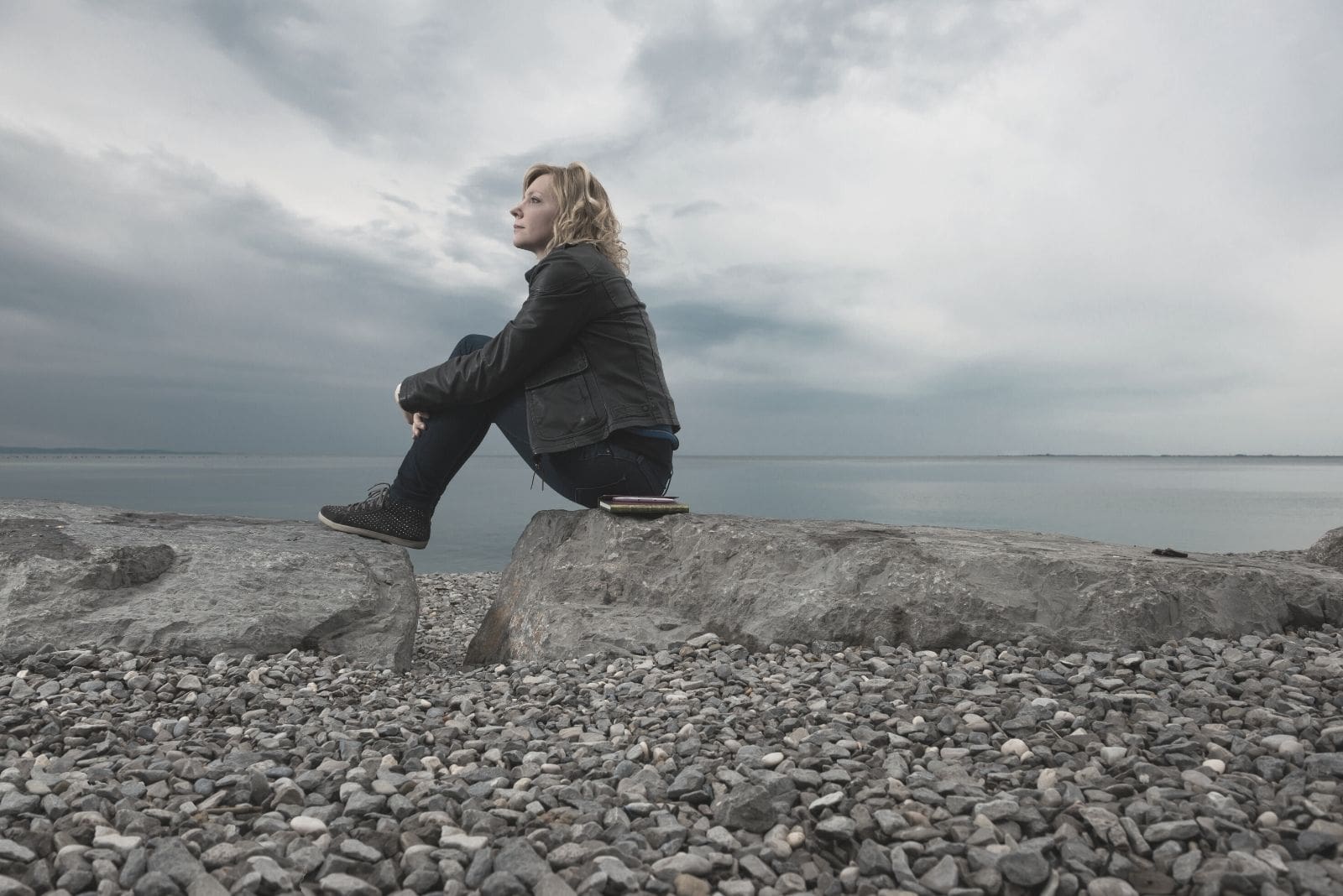 mujer soñadora y pensativa sentada en la roca de la playa 