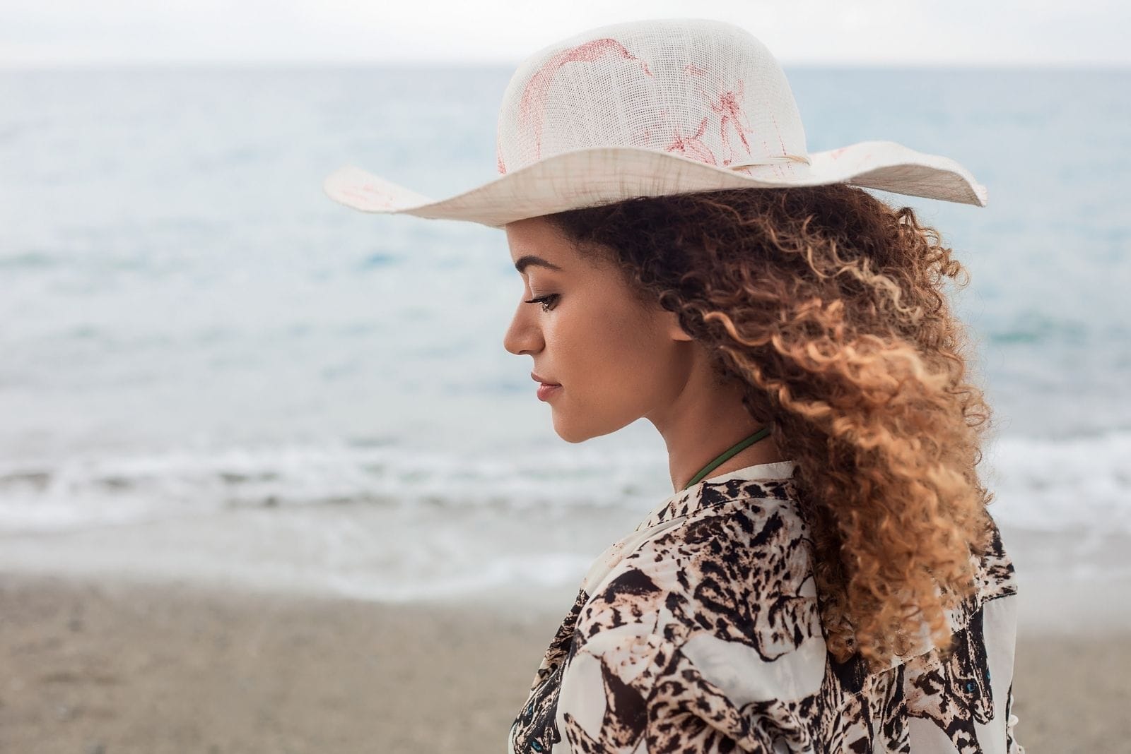 donna splendida e pensierosa in piedi vicino al mare con un cappello