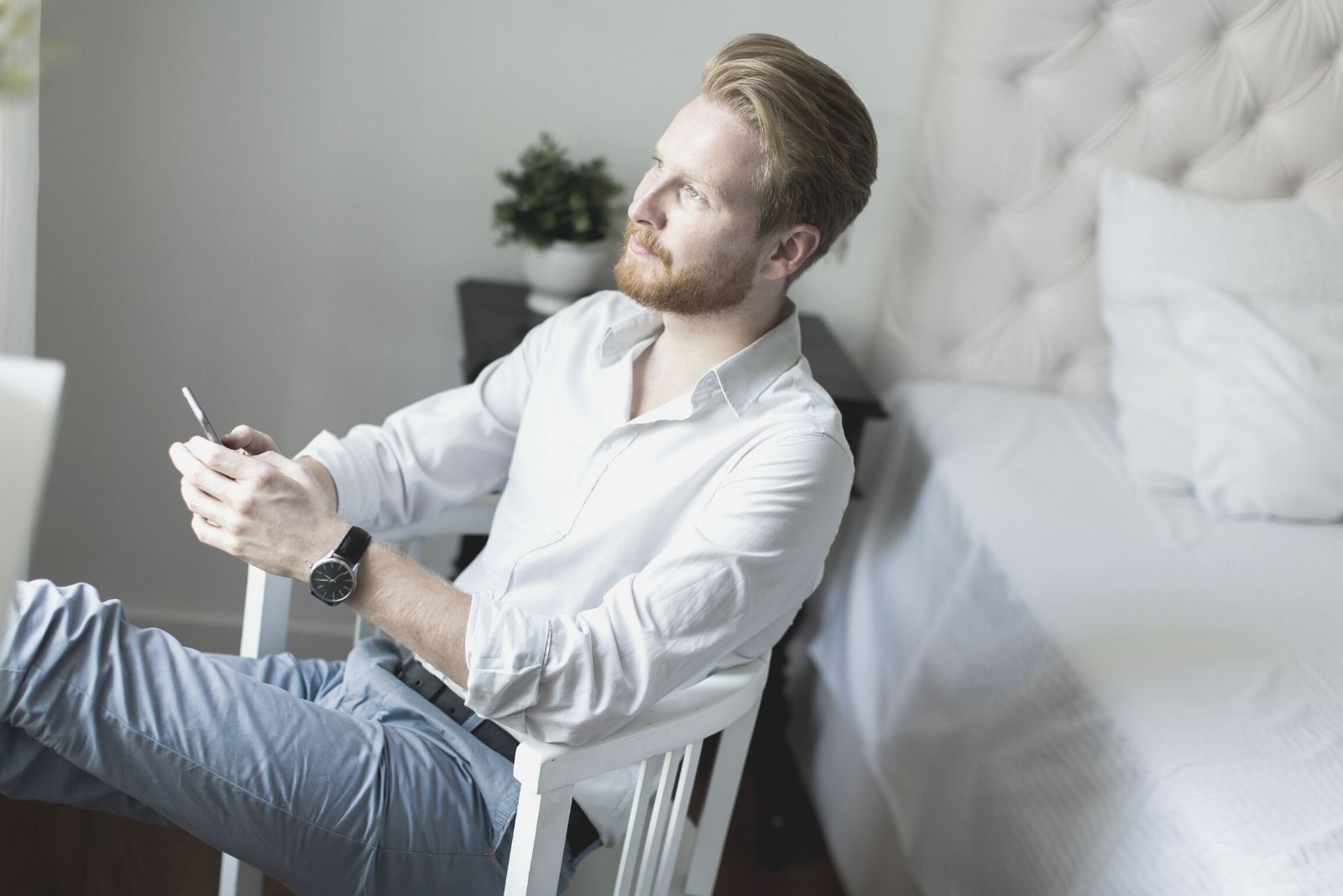 pensive man looking at a distant sitting in the bedroom's chair holding at a smartphone
