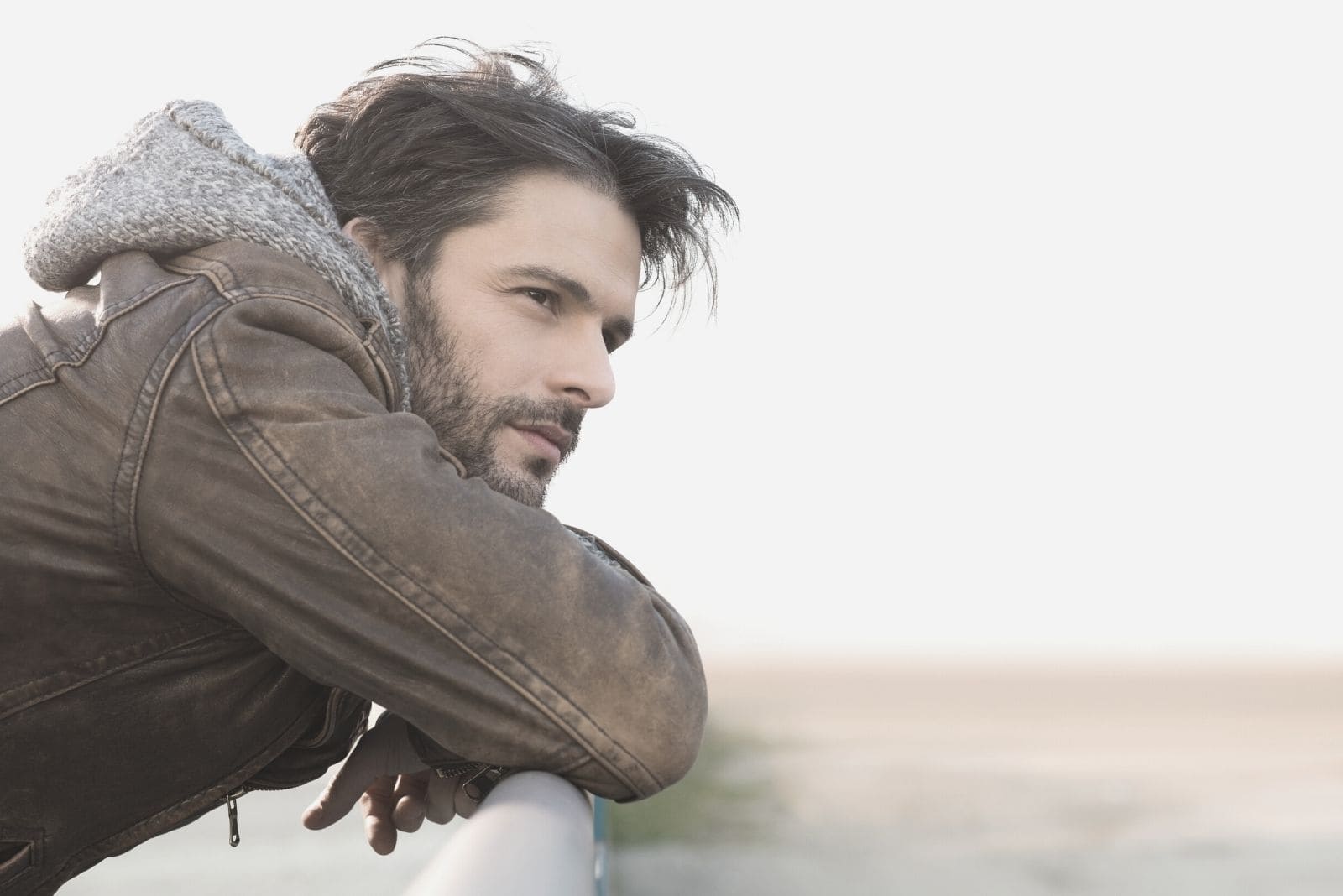 pensive man outdoors leaning on a railing wearing jacket with a hood