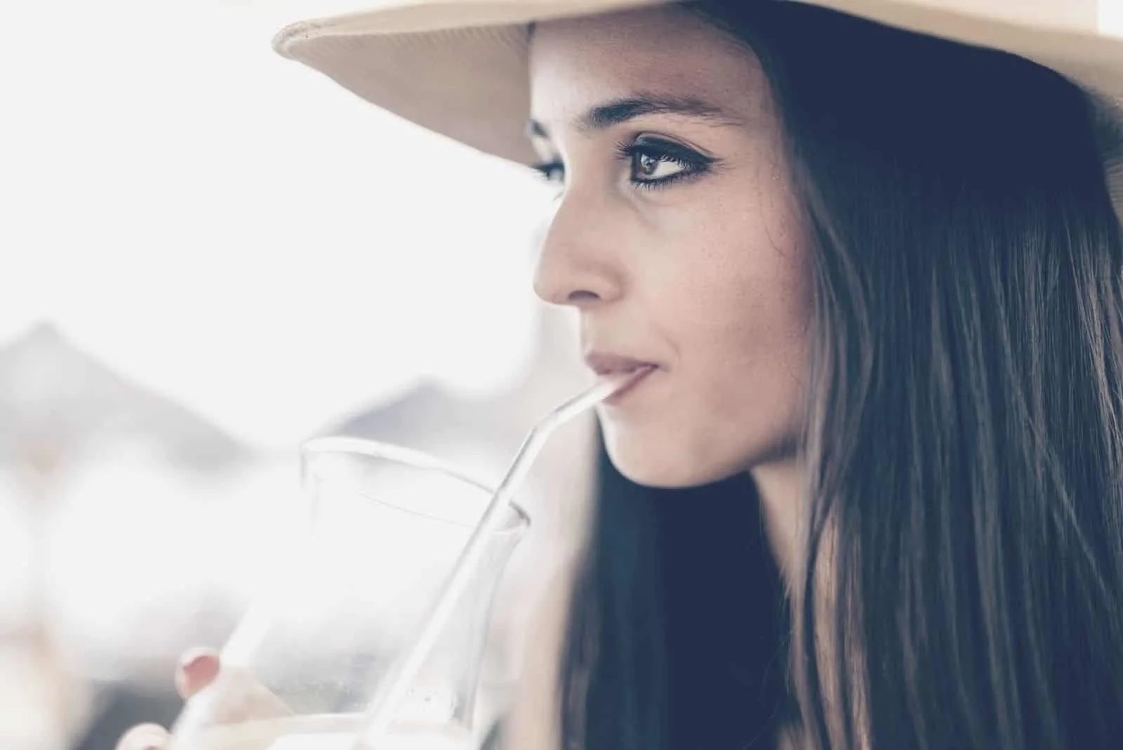 pensive woman drinking beverage in sideview close up photo wearing a hat 