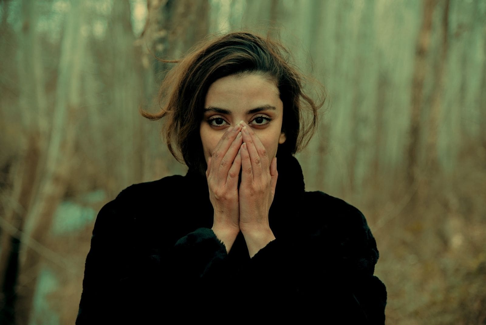 pensive woman in black coat covering her face with her hands standing outdoors