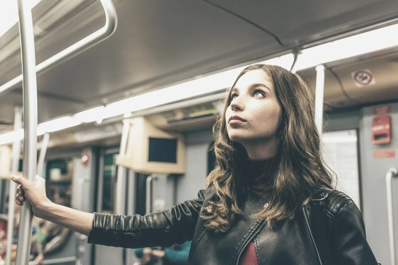 pensive woman travelling on a subway standing and holding the railing looking upwards