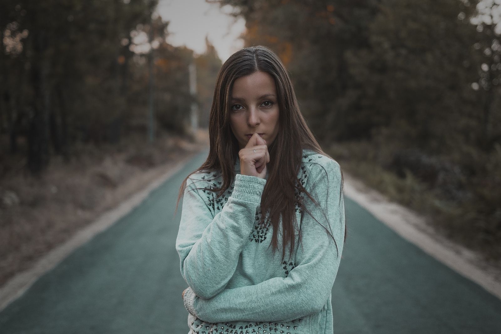 photo of a woman standing in the middle of an empty street deep thinking with hand on her lips