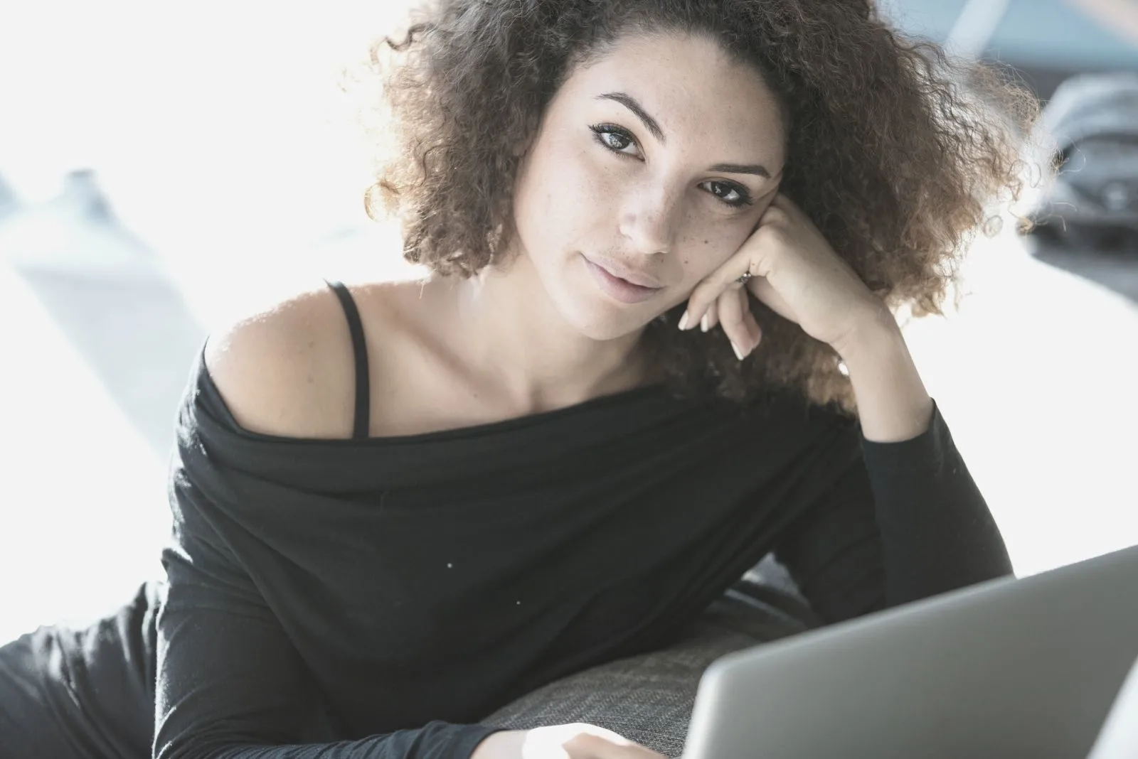 pretty curly haired woman lounging while working on laptop looking at the camera