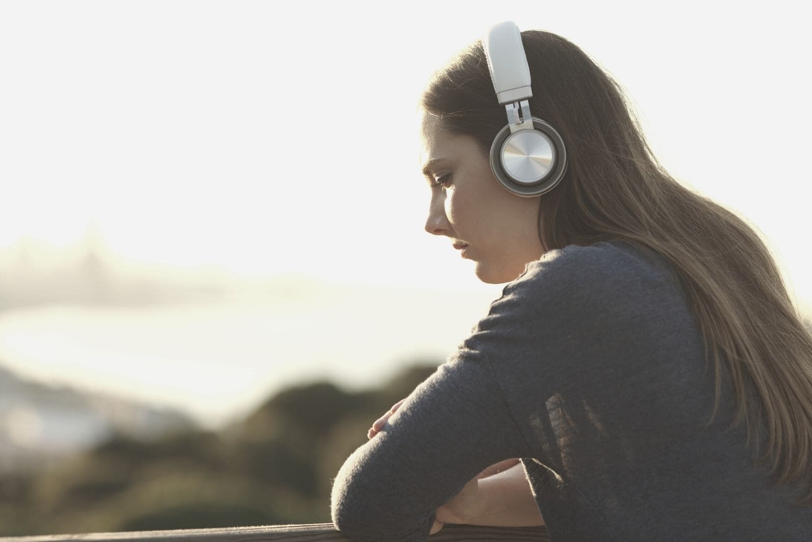 donna triste e pensierosa che ascolta la musica in cuffia su una vista semi posteriore in piedi all'aperto