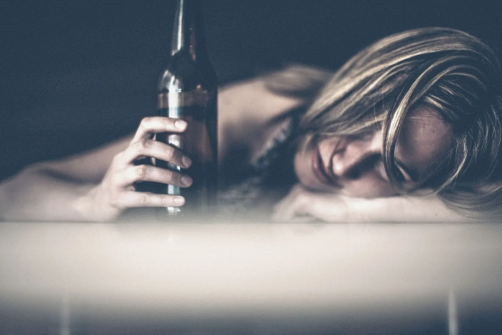 sad woman drinking and holding beer while crying and leaning her head on the table