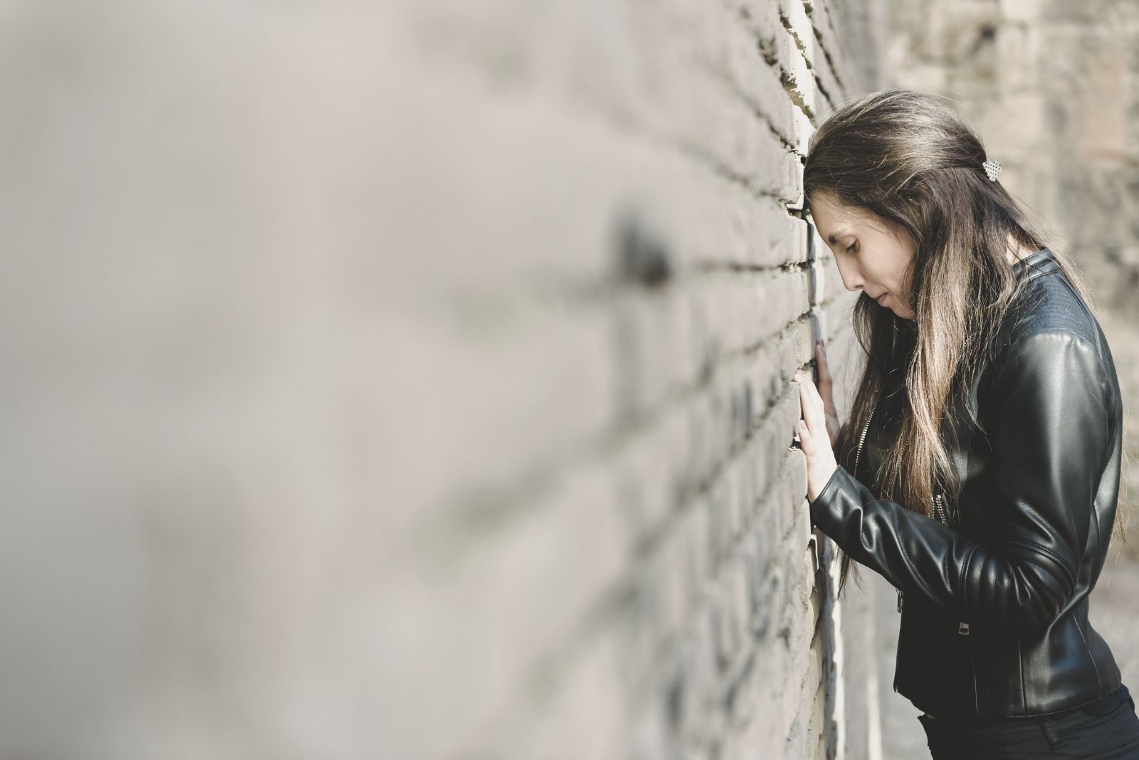 donna triste di fronte al muro di mattoni che indossa la giacca di pelle