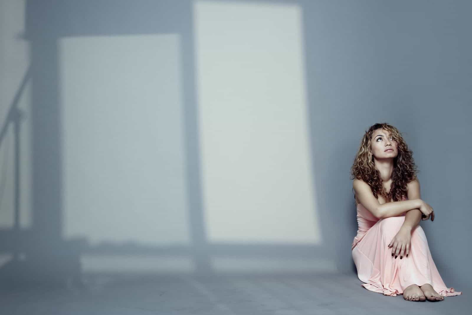 donna triste seduta sul pavimento con la luce che entra dalle finestre