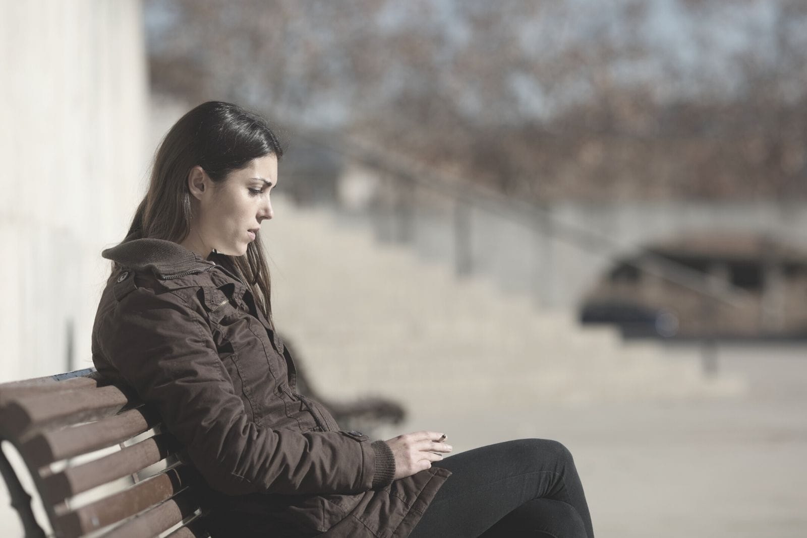 sad woman smoking on the bench in the street in winter clothes