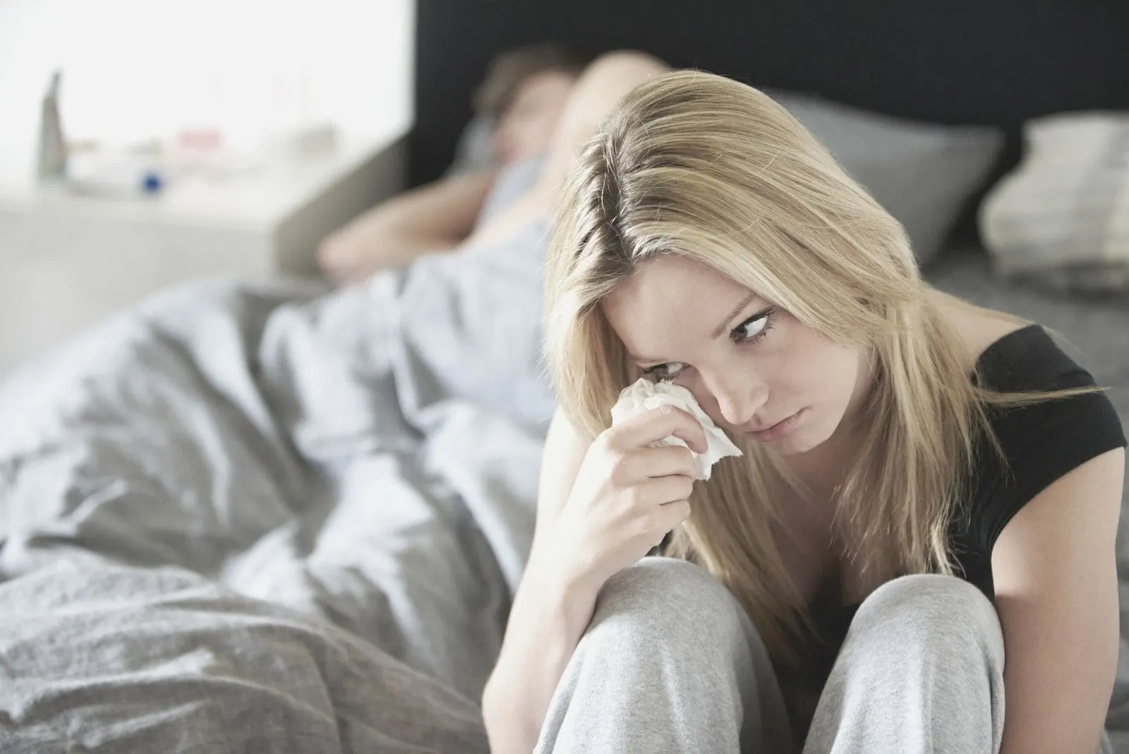 sad young girlfriend crying near sleeping boyfriend inside the bedroom