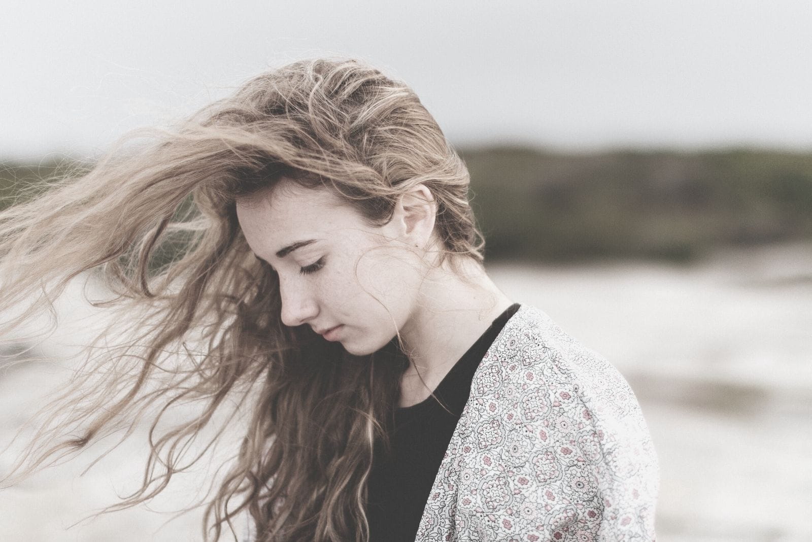 mulher jovem e triste perto da praia a caminhar com o cabelo soprado pelo ar, inclinando a cabeça