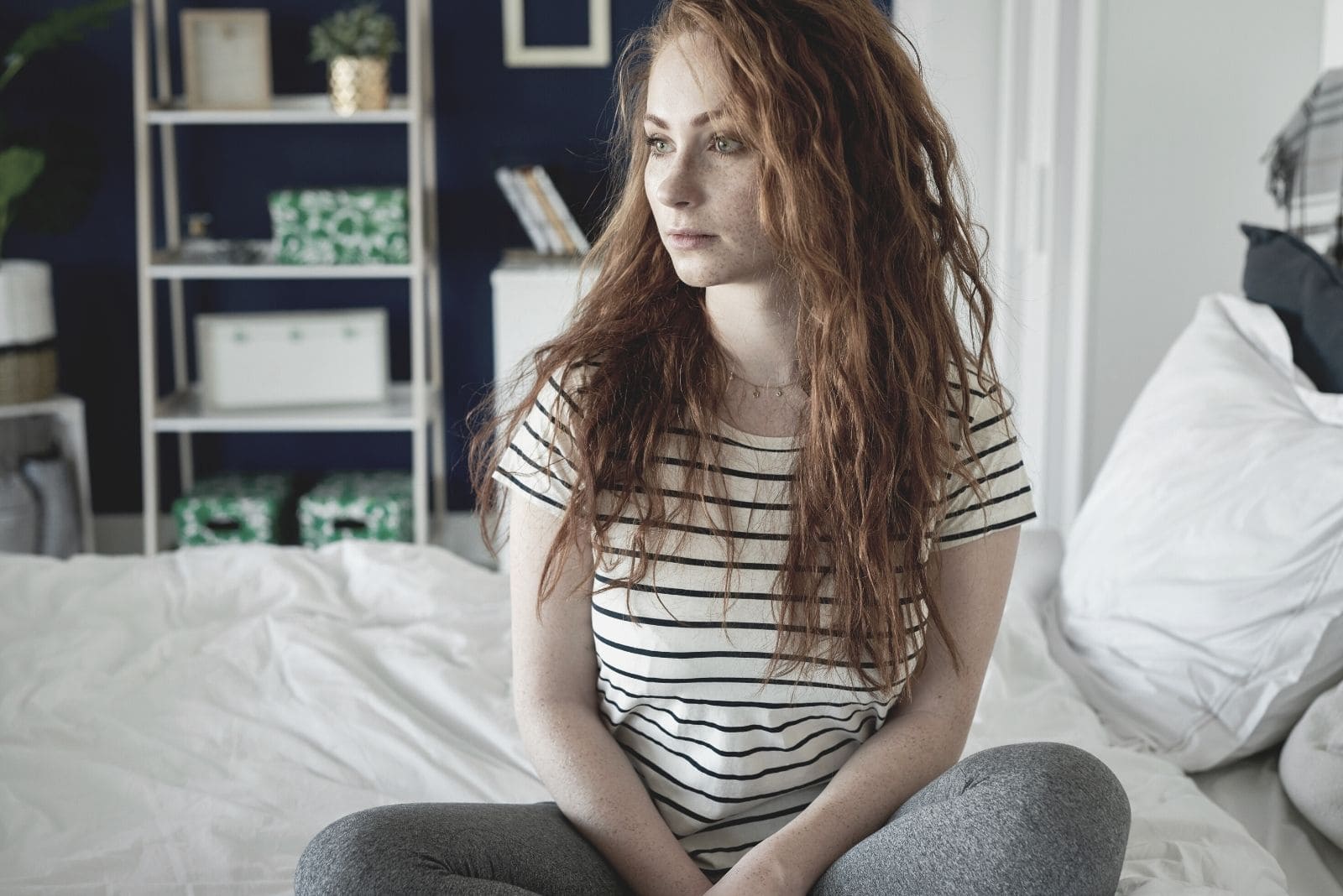 sad young woman sitting alone on bed looking away
