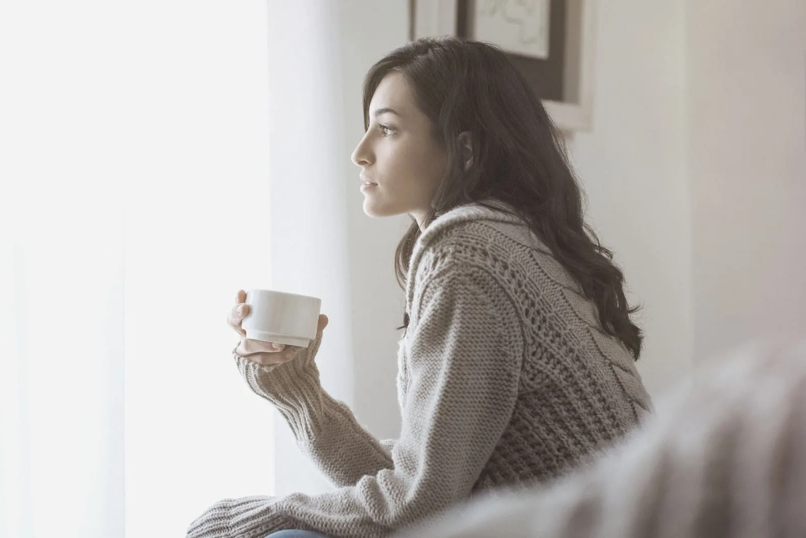 sideview of a pensive woman drinking coffee looking at the windows