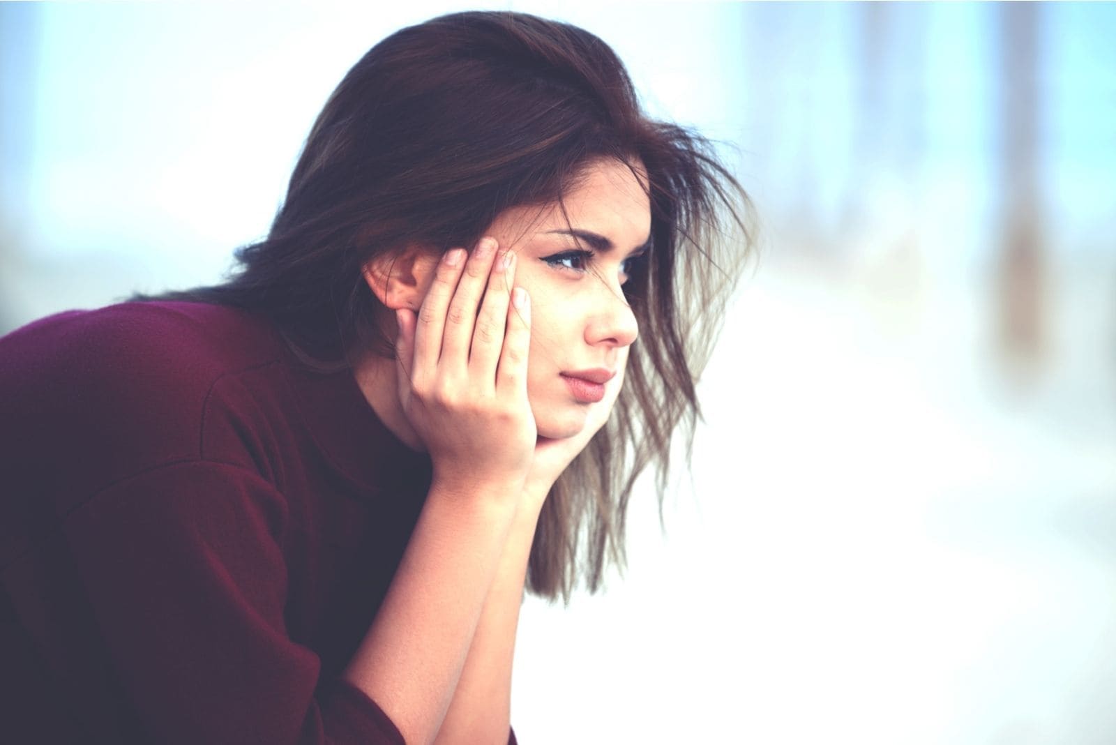 sideview of a pensive woman with two hands supporting her head and looking away