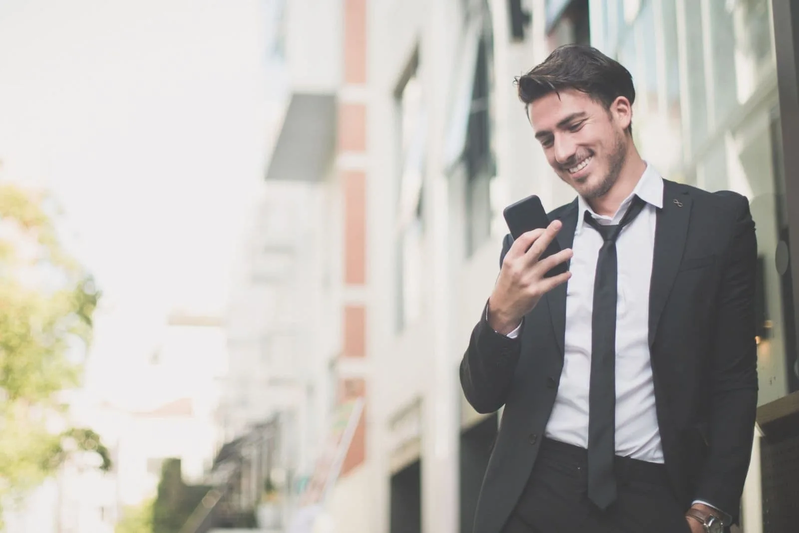 smiling business man texting with his phone leaning on the wall outdoors