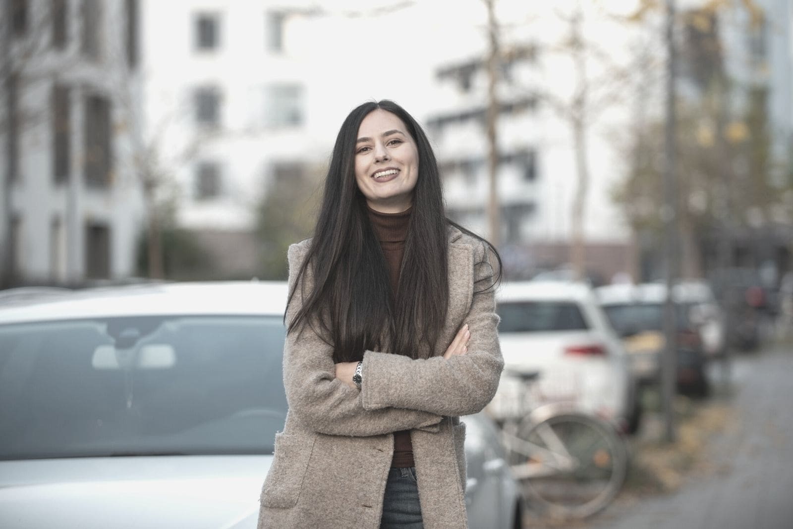 mulher sorridente ao ar livre, parada em frente ao carro estacionado na berma da rua