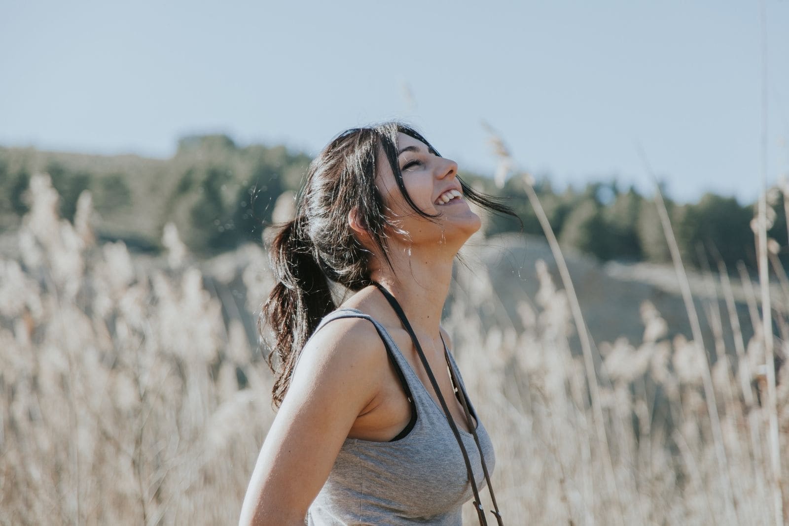 smiling young woman standing in the field closing her eyes in sideview