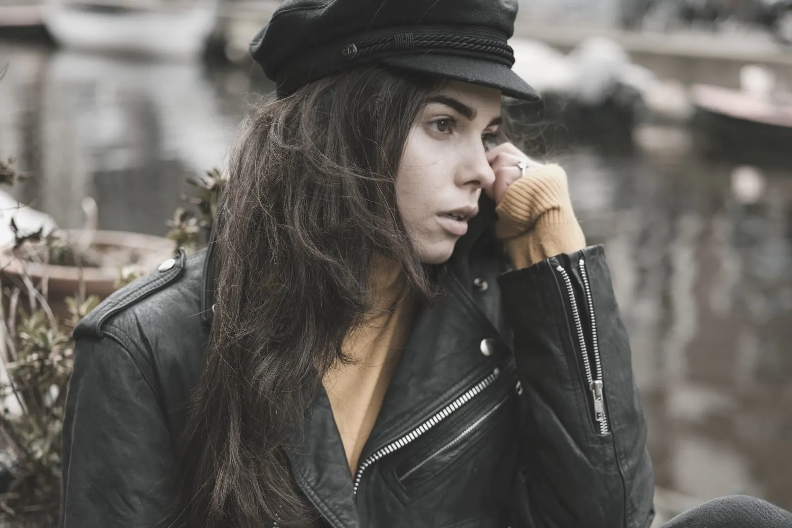 stylish pensive woman resting on a sidewalk near a canal in autumn city