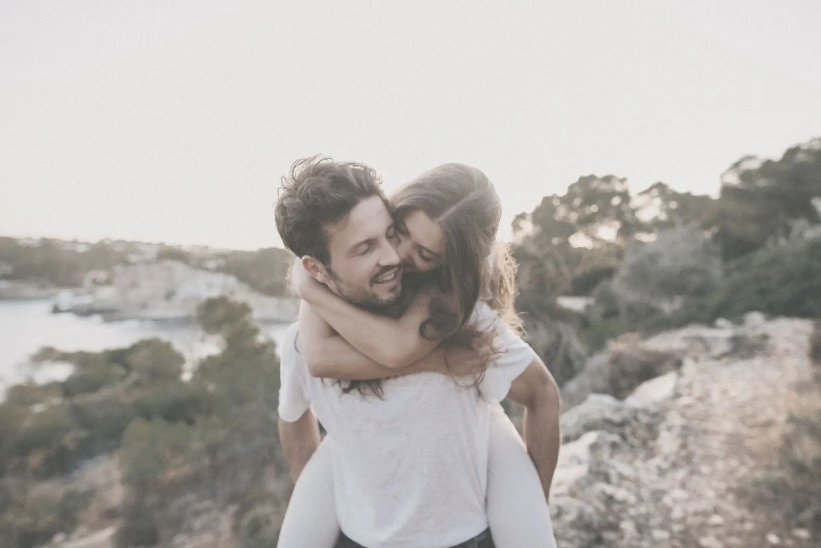 sweet couple piggy back near the body of water cheerfully