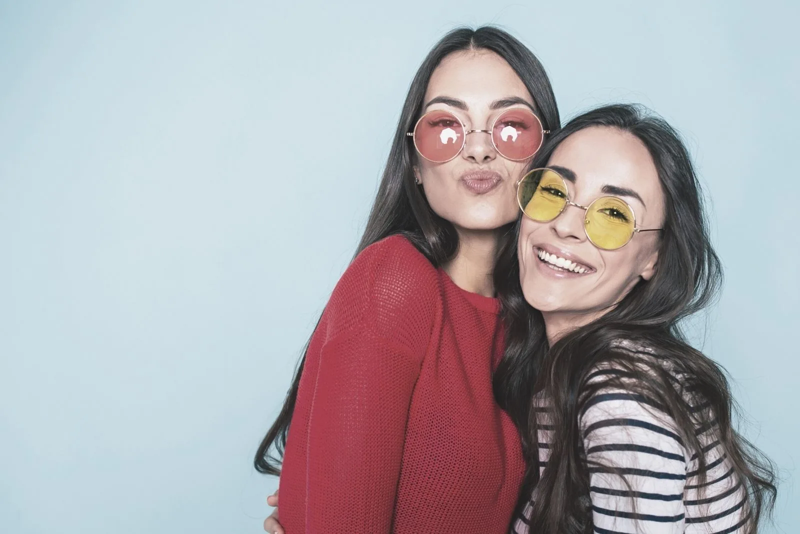 two cute lovely girls taking a pose for a picture with sunglasses in blue background