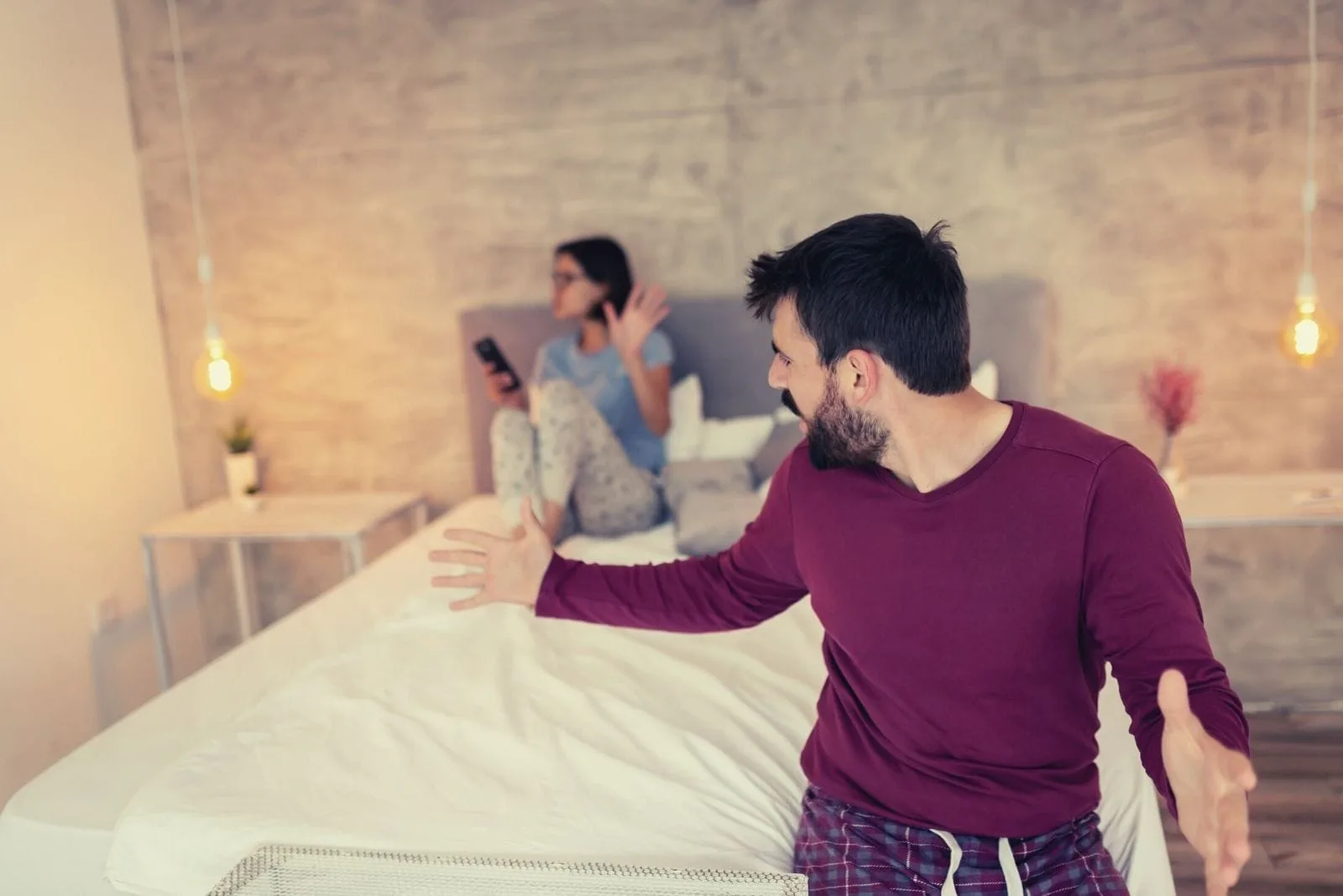 upset couple arguing in bed with the woman signing stop while looking at the smartphone