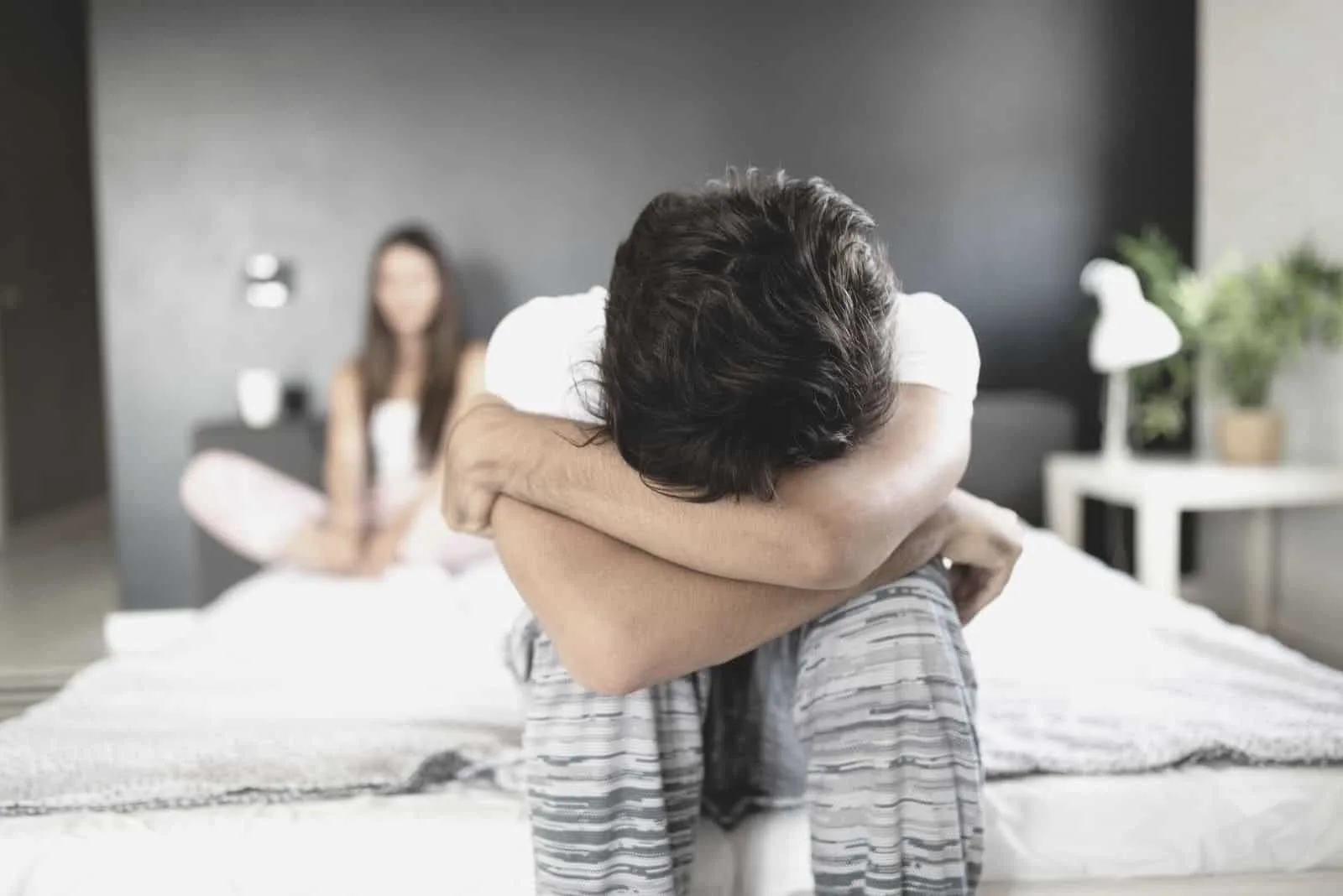 upset man in bed crying covering his face with a blurred image of a woman sitting in the same bed