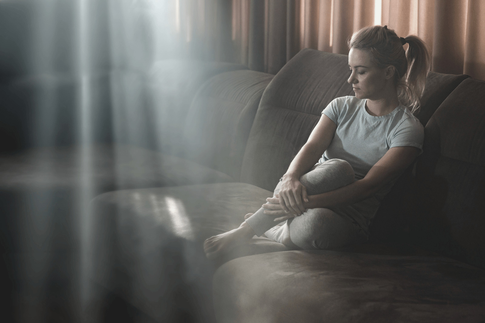 woman at home sitting on the sofa inside the closed window dark and feeling sad