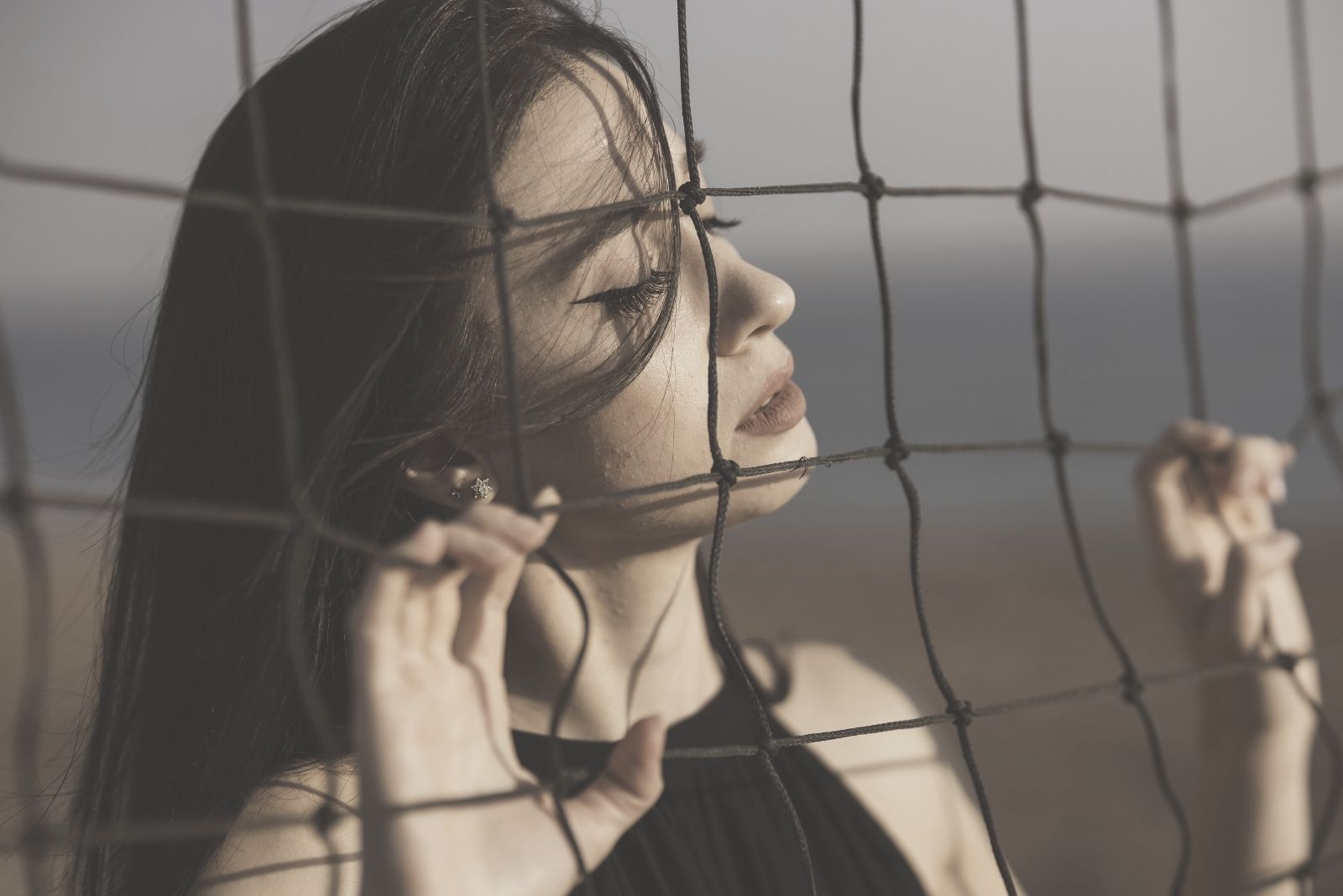 mujer cerrando los ojos mientras cerca y sosteniendo en la red vestido negro en foto de primer plano