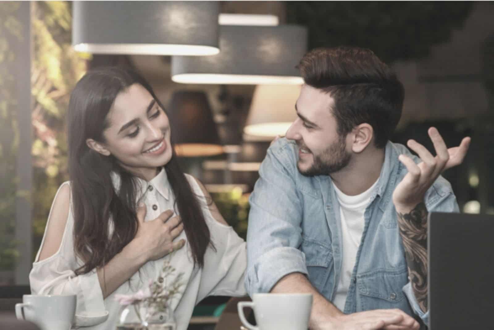 woman holding her chest and smiling while talking to a man beside her inside the cafe