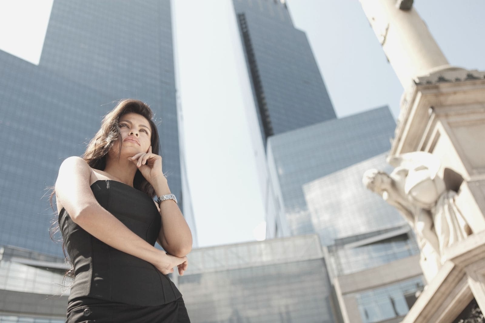 mujer con vestido negro de pie cerca de los rascacielos pensando en ángulo bajo
