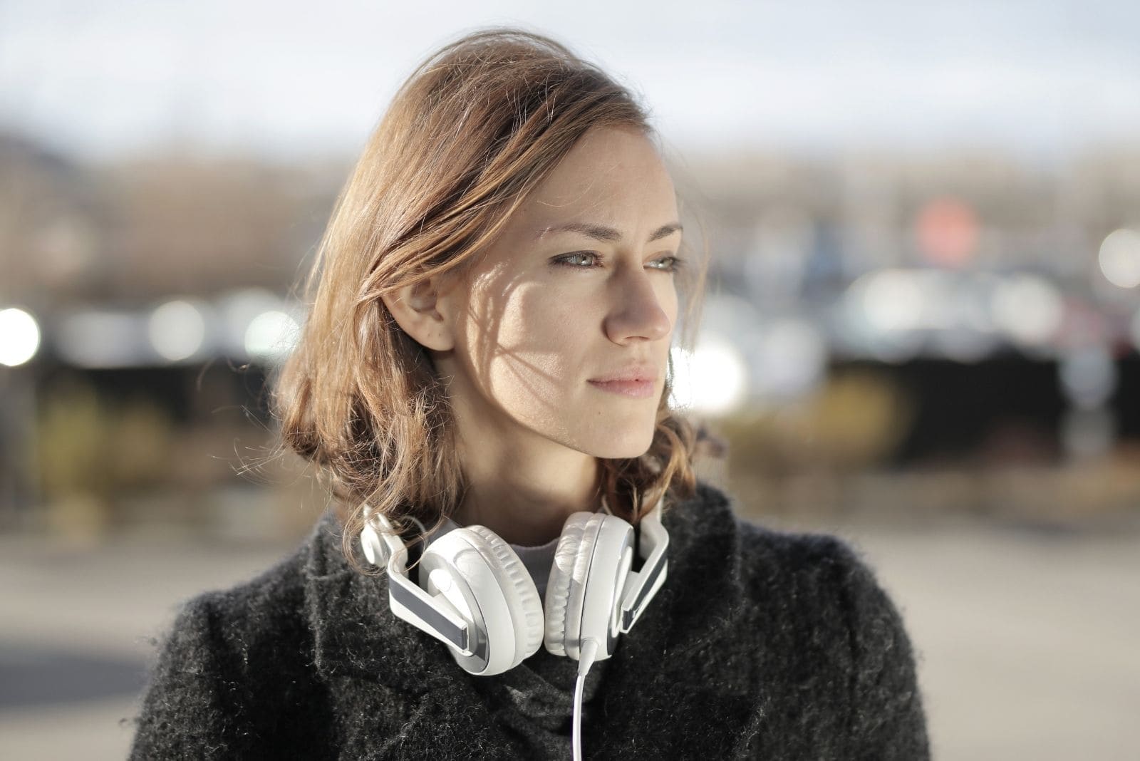 woman in black fur coat and big white headphones staring away pensively outdoors