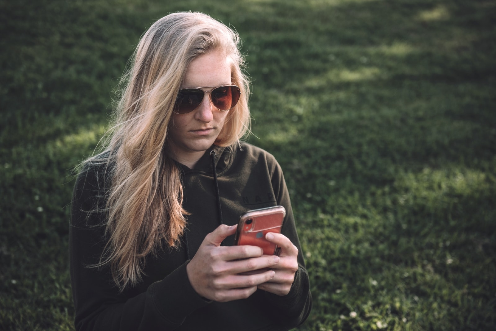 blonde woman with sunglasses looking at phone outdoor