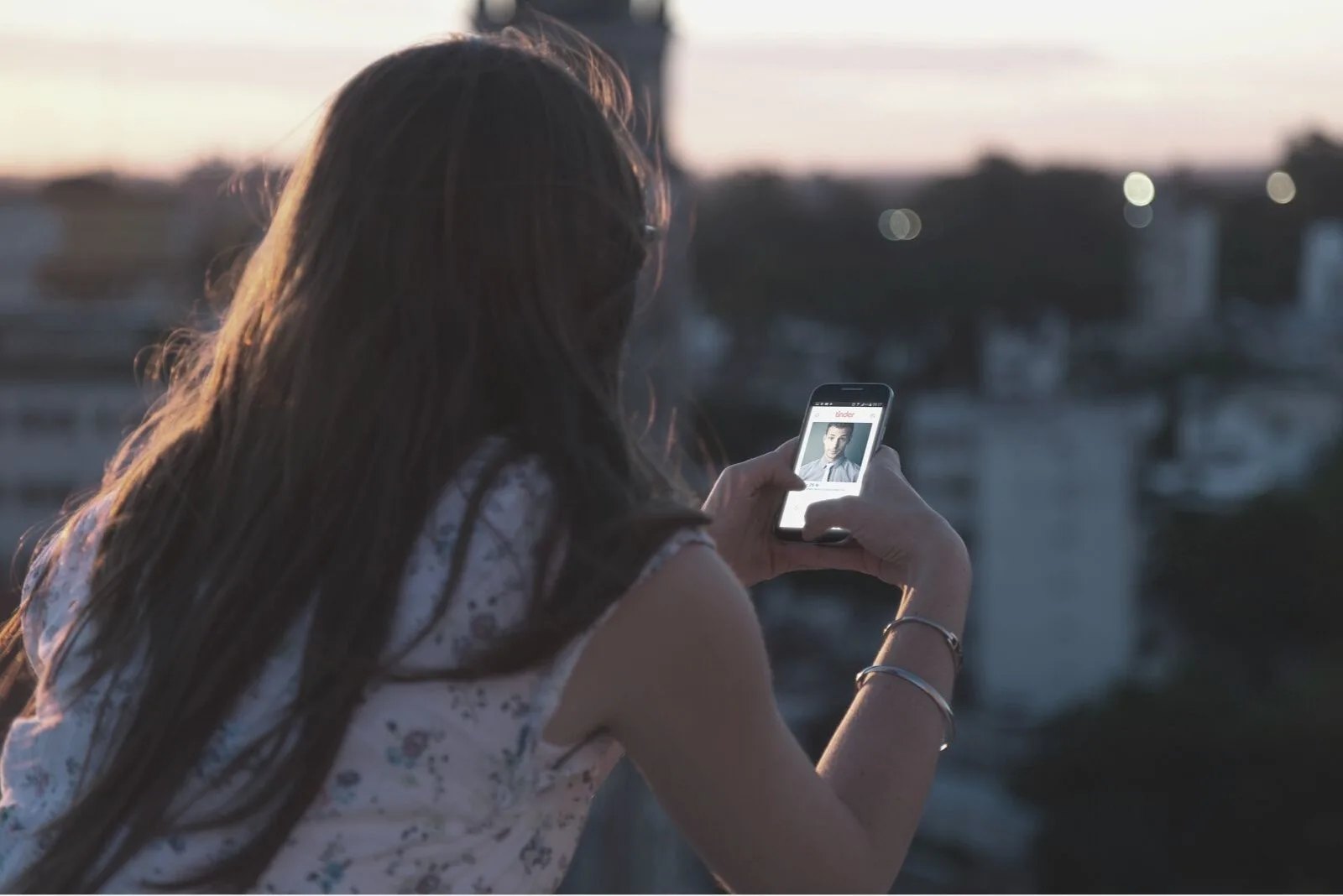 woman looking at picture of a man in her phone standing at rooftop