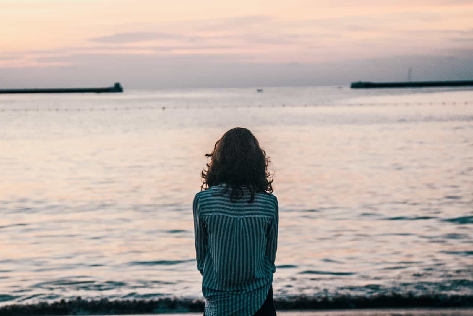 woman in striped shirt looking at sea during sunset