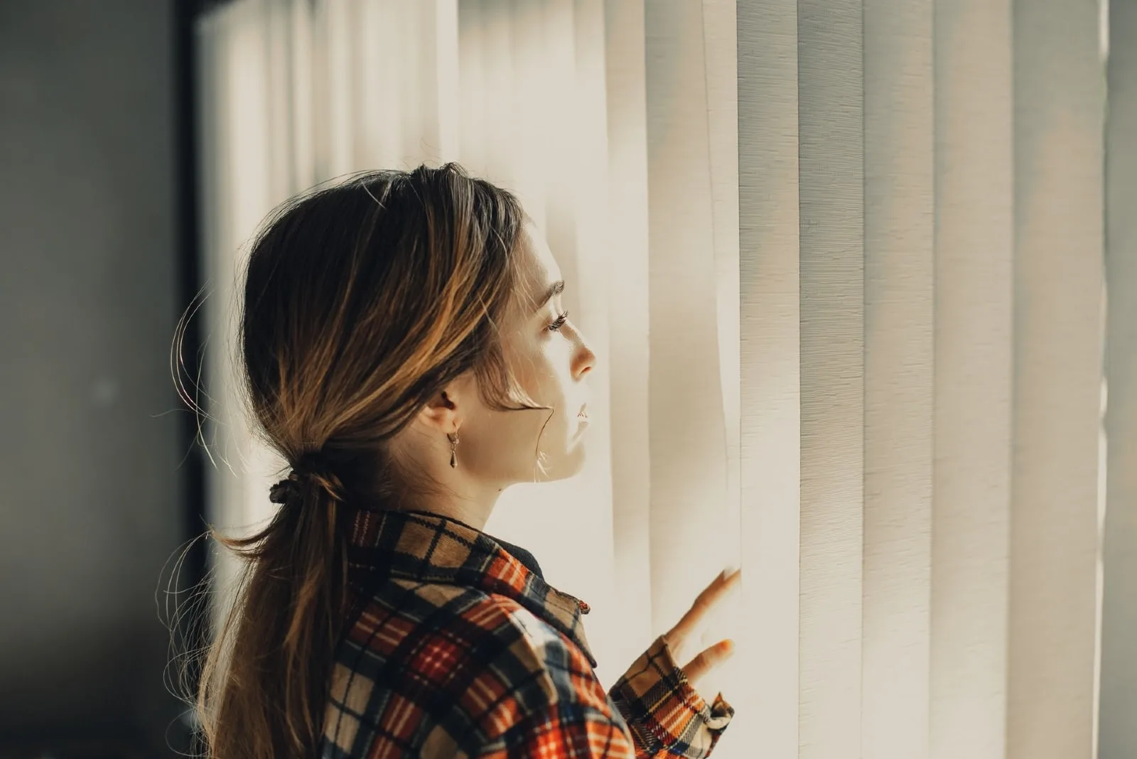 pensive woman in checked shirt looking through window
