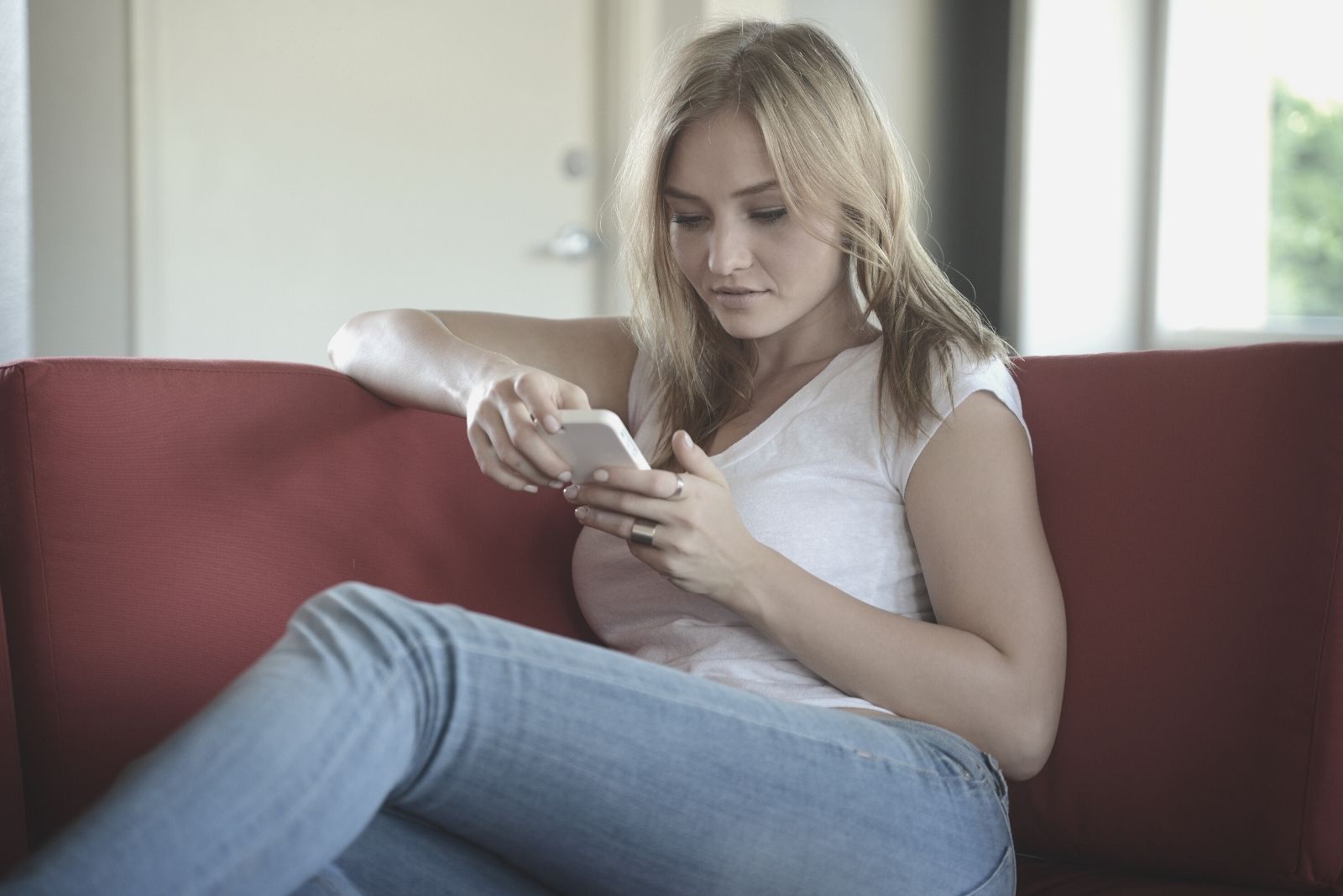 woman looks intently at her phone and relaxing on the red couch inside livingroom