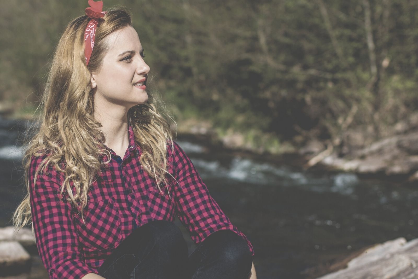 woman meditating near waterfall sitting on the rock wearing a red cloth head band