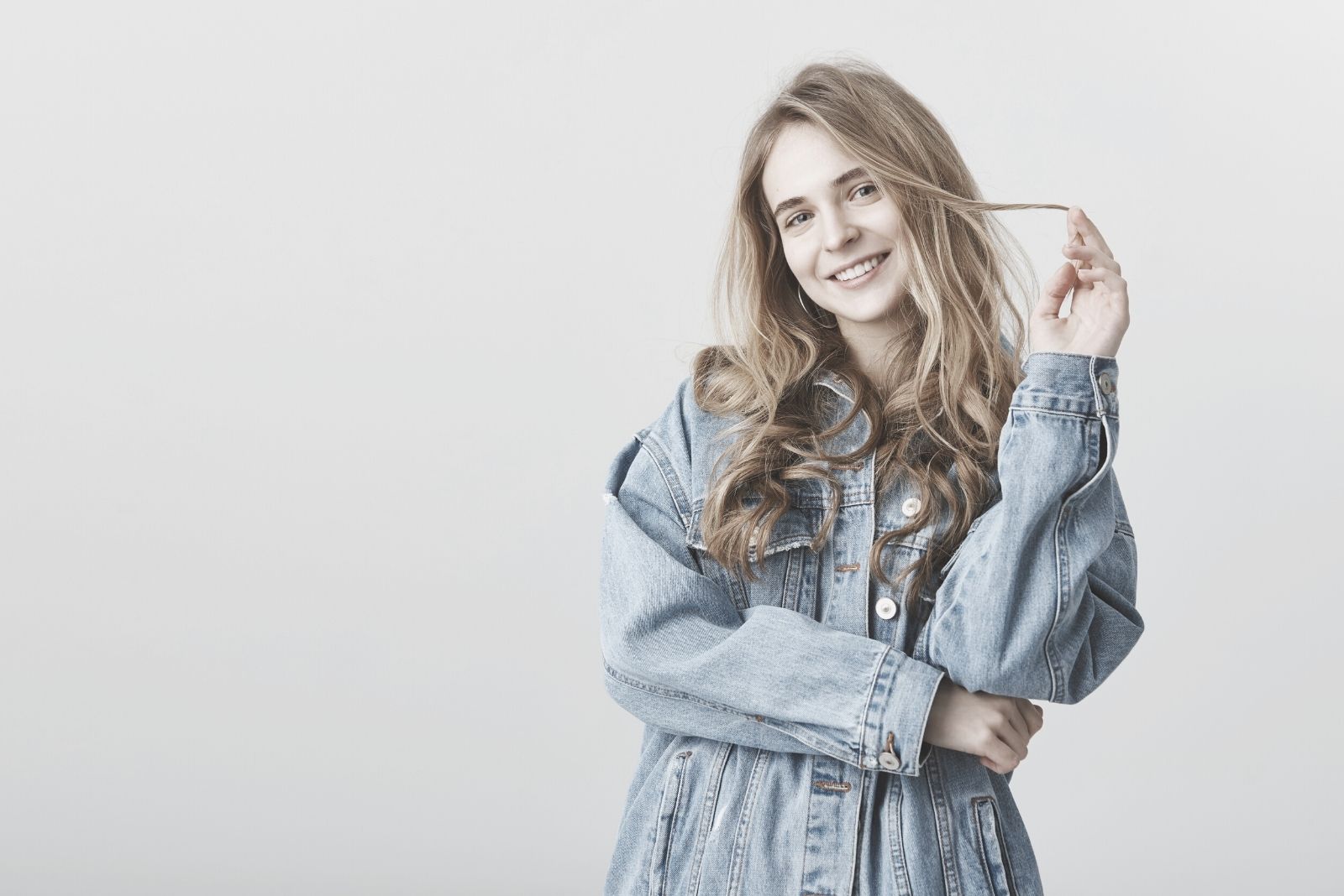 woman playing with her hair standing and wearing large denim jacket