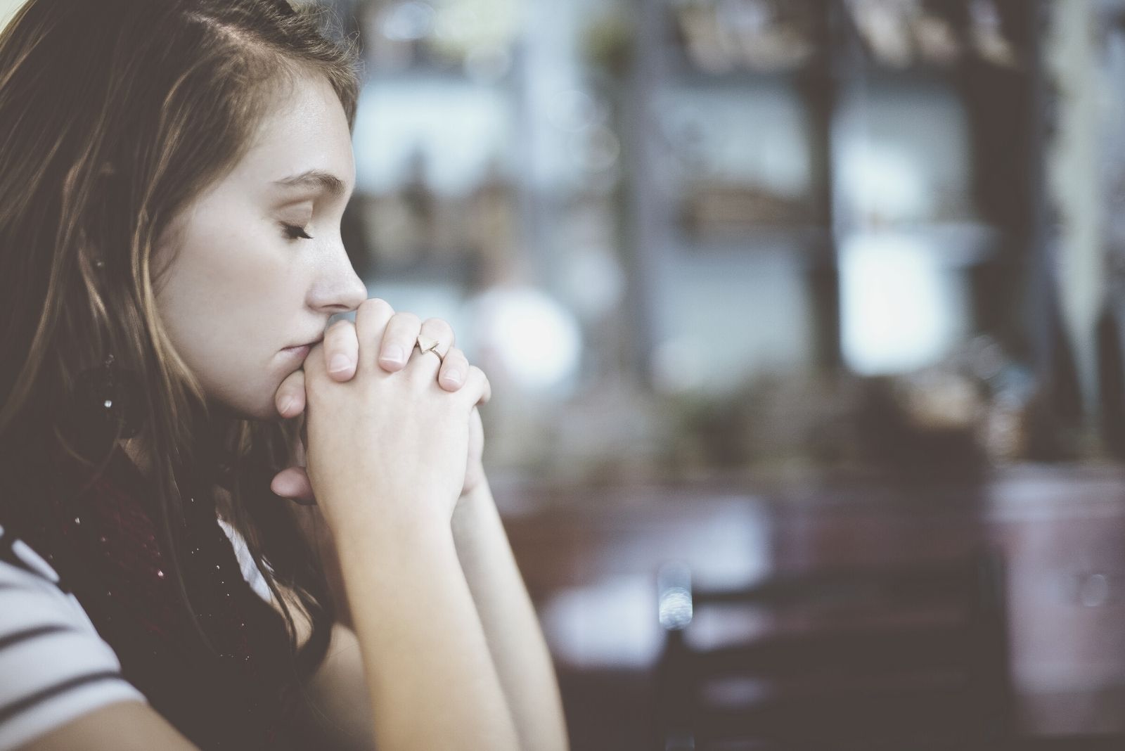 woman praying indoors in sideview with close fist near the face