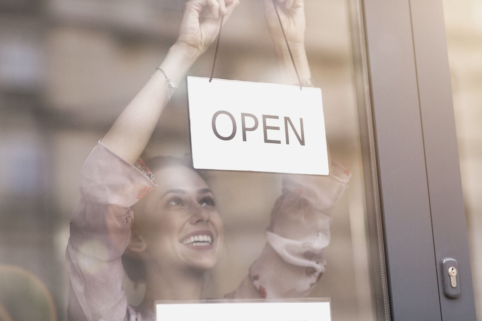 mujer colocando cartel de abierto en la puerta principal de un establecimiento