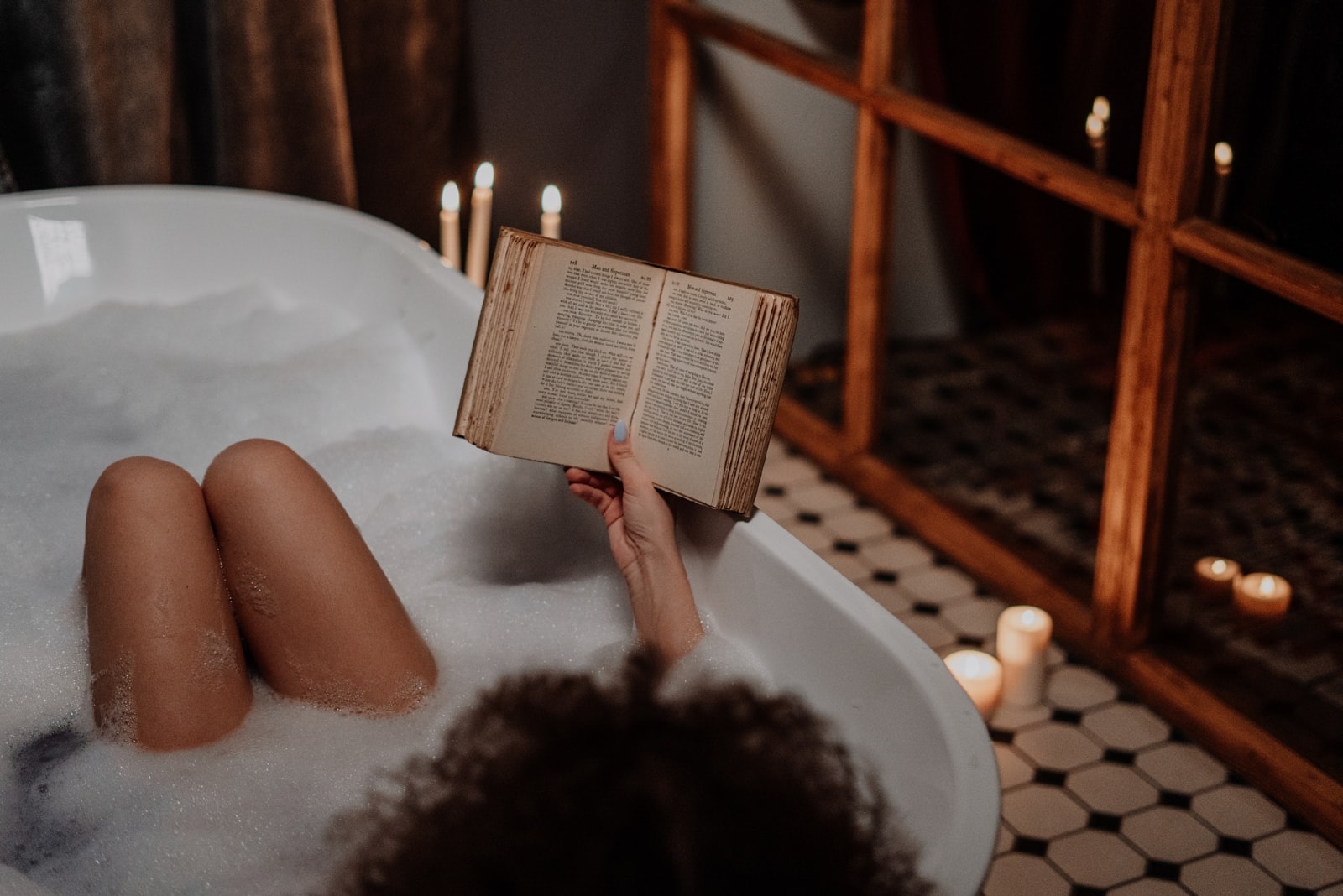 woman reading book while sitting in bathtub