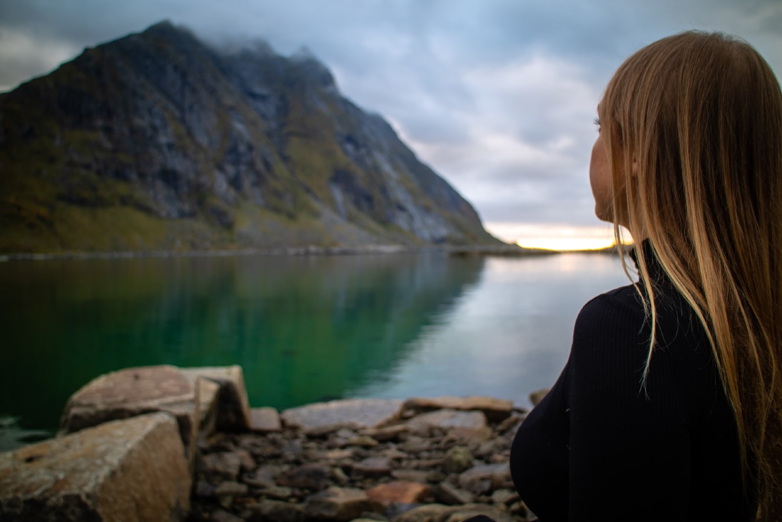 donna con maglione nero a collo alto seduta vicino al lago