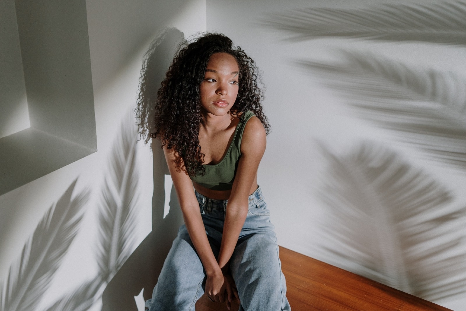 woman with curly hair sitting near wall