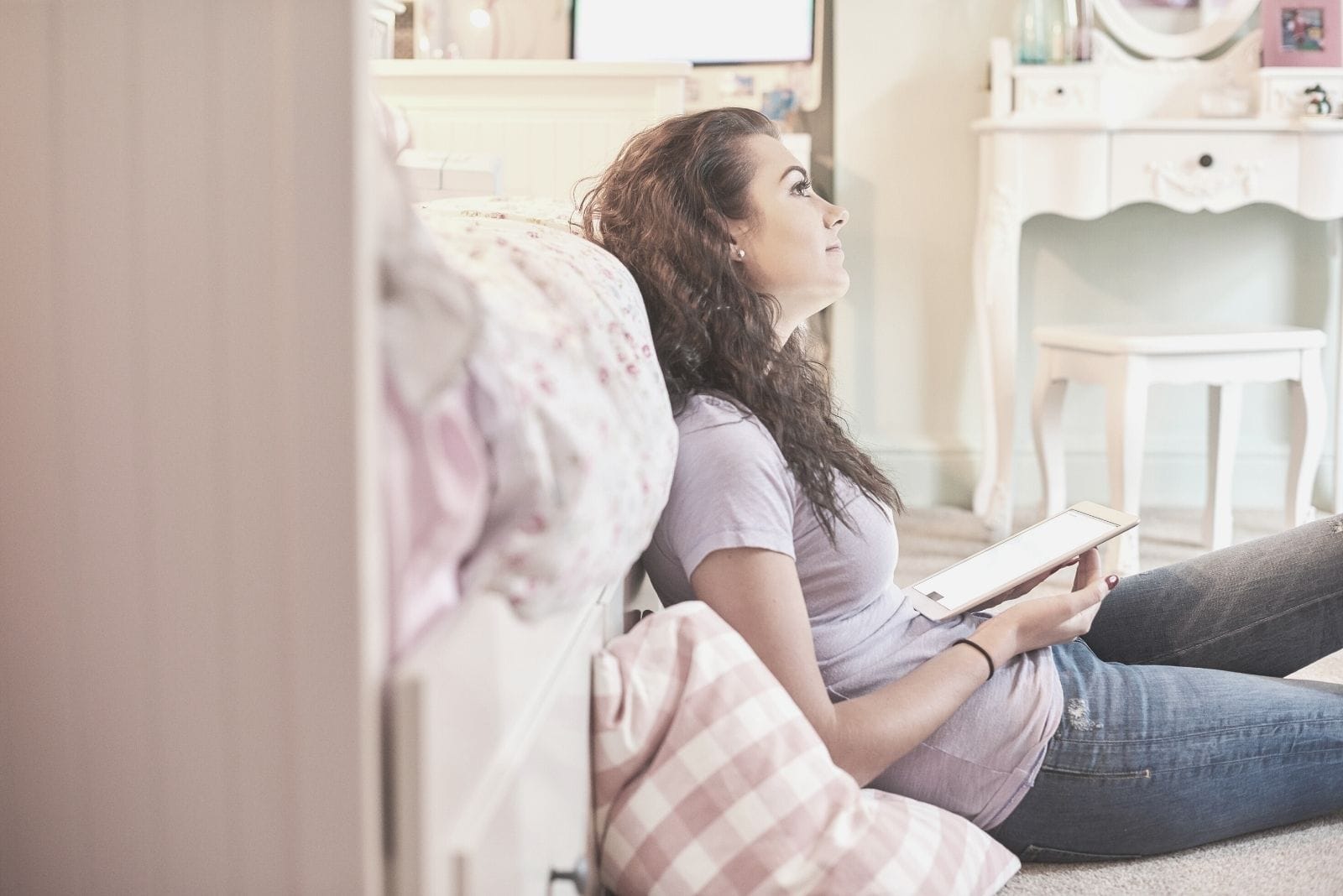 mujer sentada junto a la cama pensando mientras sostiene un gadget